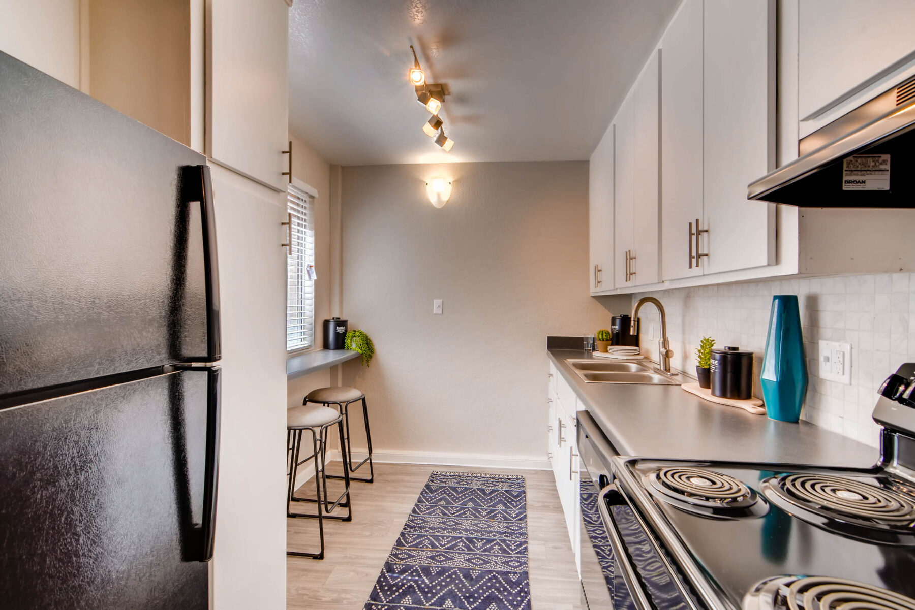 Apartment kitchen with bar seating, cabinets, drawers, natural lighting, and black appliances